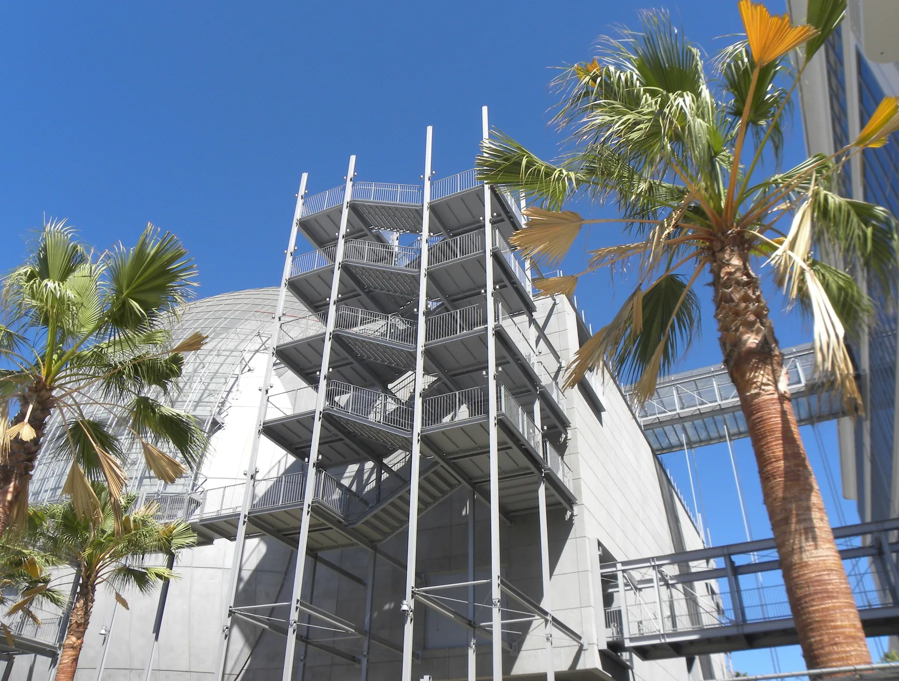 Exterior steel stair tower beside the spherical theater of the Academy Museum of Motion Pictures, framed by palm trees